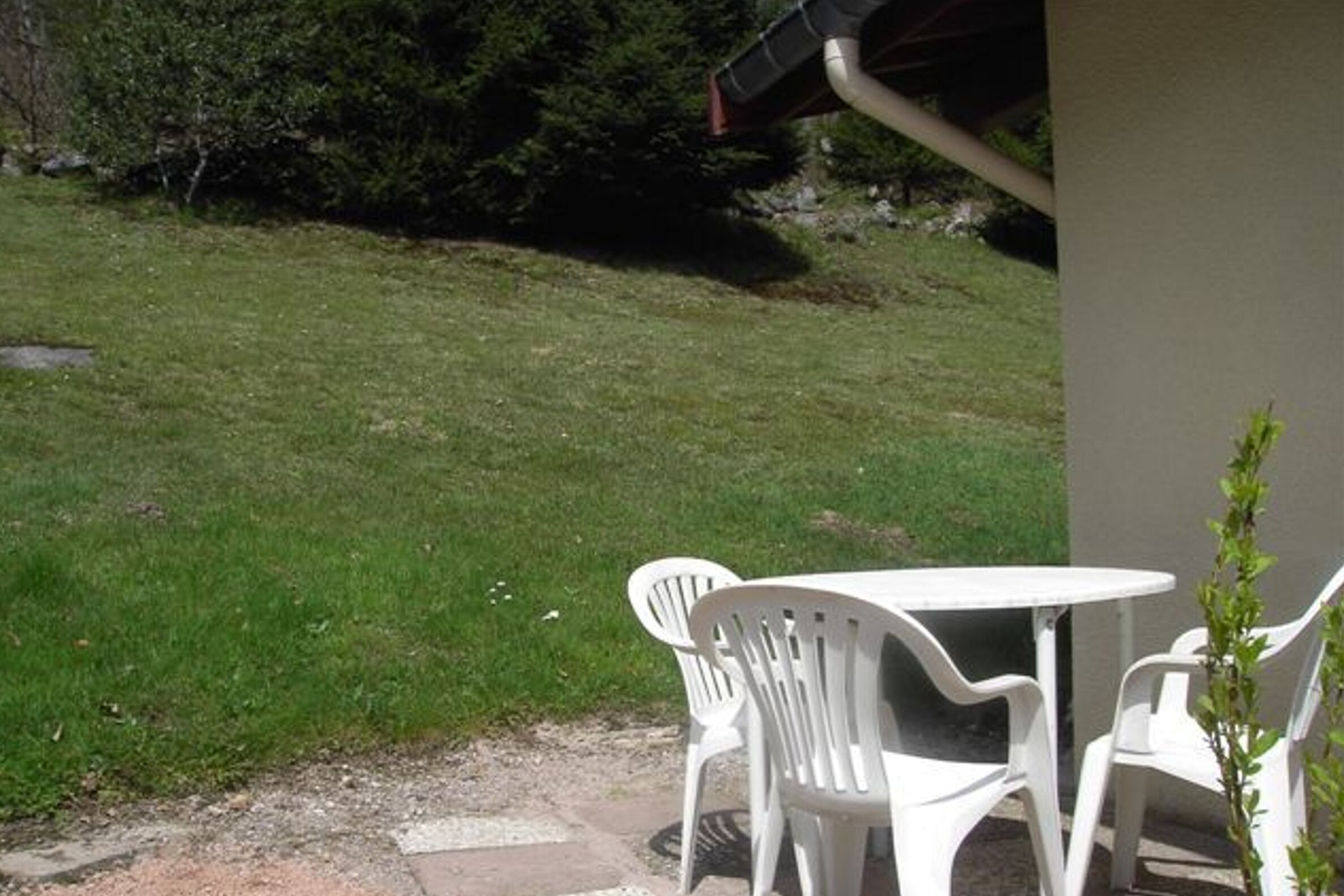 Eine Terrasse mit einem runden Tisch und vier weißen Plastikstühlen.
