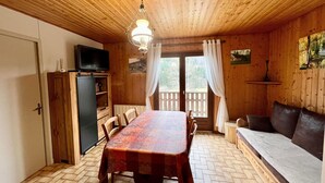 A wooden interior with a dining table, chairs, a sofa, a television, and a refrigerator. - Chalet en Forêt Hautes-Vosges avec Terrasse, Proche Gérardmer, 2 Chambres, WiFi, Équipements Complets (Rochesson)