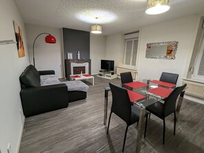 Moderni olohuone, jossa on sohva, lasinen ruokapöytä tuoleineen, takka ja televisio.