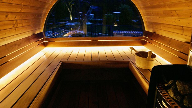 A wooden sauna with a bench and a bucket, and a view of a snowy landscape through a semi-circular window. - Magnificent Retreat in Vosges: Sauna, Hot Tub, Park, and More! (Colroy-la-Grande)
