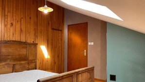 A bedroom with a wooden headboard, a bed, a skylight, a wooden door, and a patterned wall.