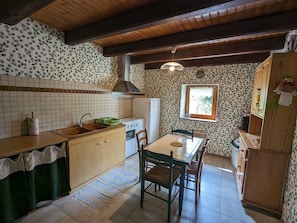 A compact kitchen with a wooden countertop, a sink, a stove, and a dining table with chairs.