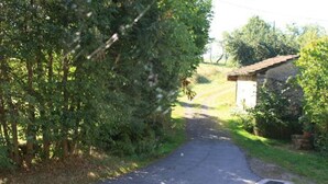 A rural road leading to a stone building with a sloped roof.