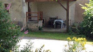 A rustic outdoor seating area with a stone bench, a table, and chairs.