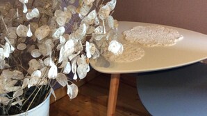 A white table with a blue chair, a white pot with dried flowers, and a wooden floor.