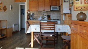 A compact kitchen with wooden cabinets, a microwave, and a dining area with a table and chairs. - T2 Apartment at the foot of the slopes with parking (Les Angles)
