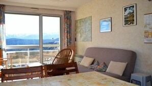 A room with a sofa, a dining table, and chairs. There is a window with a view of mountains. - T2 Apartment at the foot of the slopes with parking (Les Angles)