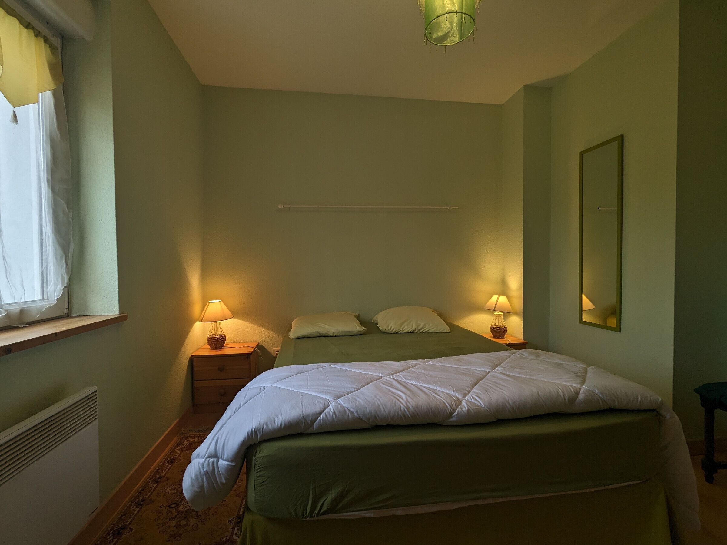 Ein Schlafzimmer mit einem Bett, zwei Nachttischlampen, einem Spiegel und einem Fenster mit Vorhängen.