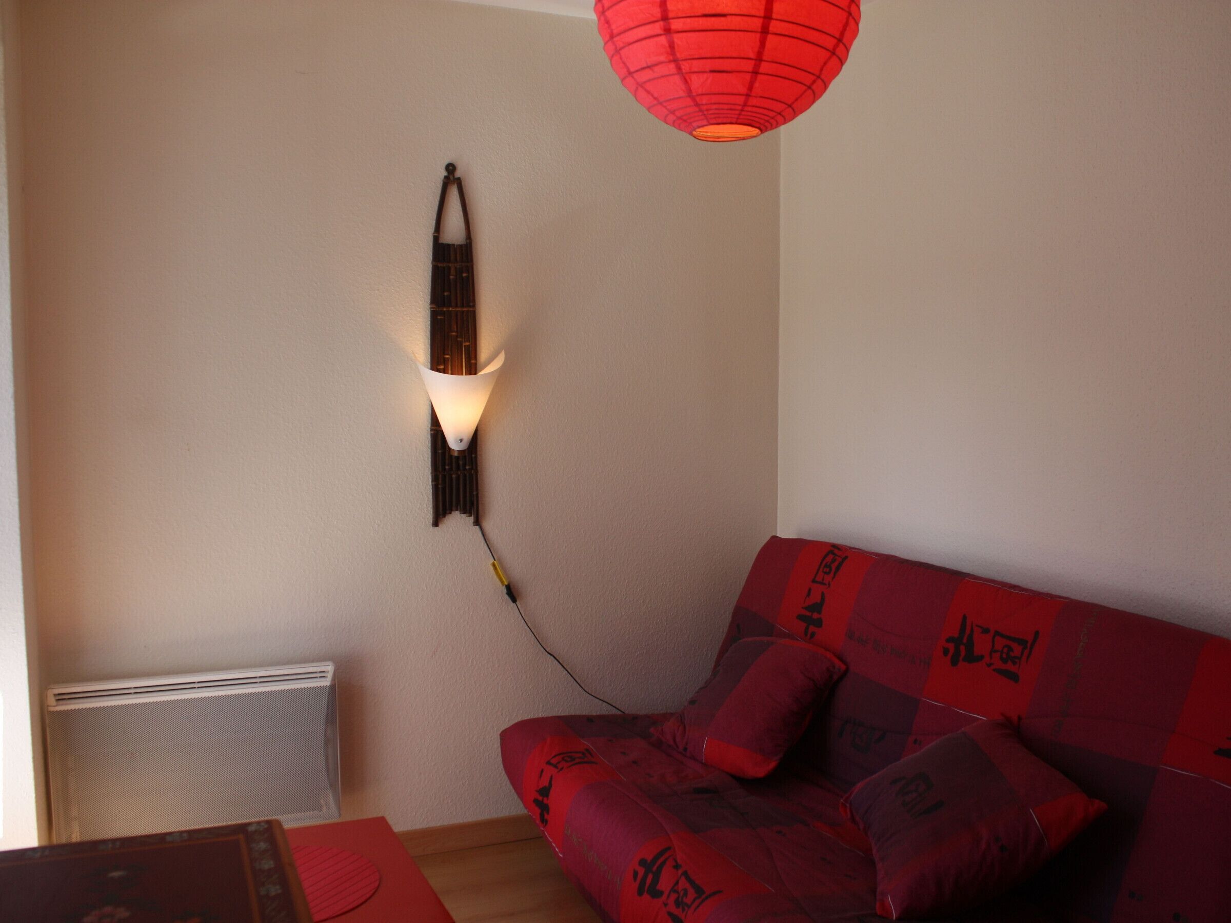 Een kamer met een rode bank, een wandlamp en een radiator.