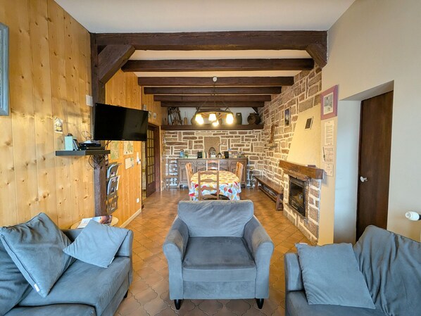 A cozy room with wooden walls, a fireplace, a dining area, and two grey sofas.
