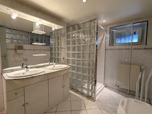 A bathroom with two sinks, a glass shower enclosure, a toilet, and a TV mounted on the wall.