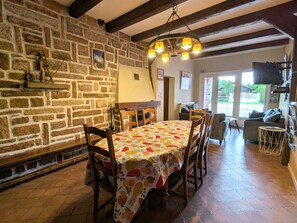 A dining area with a stone wall, wooden beams, a fruit-patterned tablecloth, and a chandelier.
