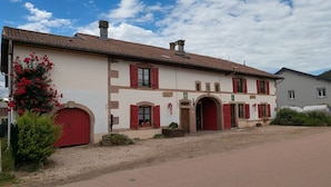 A two-story building with red doors and windows, a tiled roof, and a gravel driveway. - Spacious Rustic Cottage with Terrace, Close to Gérardmer – Ideal for Families (Granges-Aumontzey-Aumontzey)