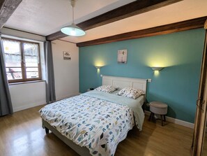 A bedroom with a bed, two bedside lamps, a window with curtains, and a small stool.