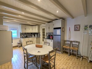 A kitchen with a dining table, chairs, a refrigerator, and a window.