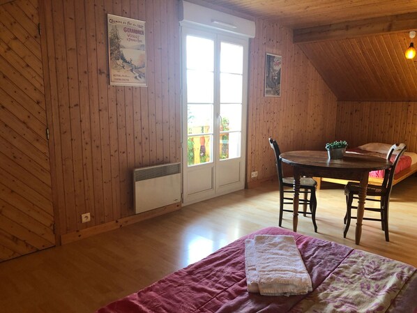 A cozy room with wooden walls, a bed with a pink blanket, a table with chairs, and a radiator. - Spacious chalet with balcony, free WiFi, close to lake and ski resort (Gérardmer)