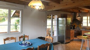 A kitchen with wooden beams, a stainless steel refrigerator, and a dining area with a blue tablecloth.