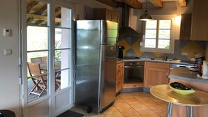 A kitchen with a stainless steel refrigerator, wooden cabinets, a dishwasher, and a small round table with a bowl.