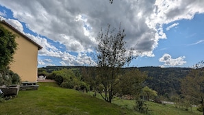 Et hus med terrasse og udsigt til en skovklædt bakke.