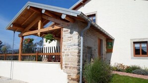 Un bâtiment en pierre doté d’un porche en bois et d’un petit jardin.