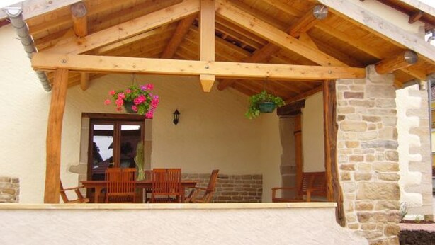 Une véranda en bois avec un mur en pierre, une table en bois avec des chaises et des jardinières suspendues.