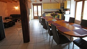 Un vaste espace de vie comprenant une table à manger, des chaises et un canapé. On aperçoit, au fond, une cuisine équipée de meubles et d’appareils électroménagers.