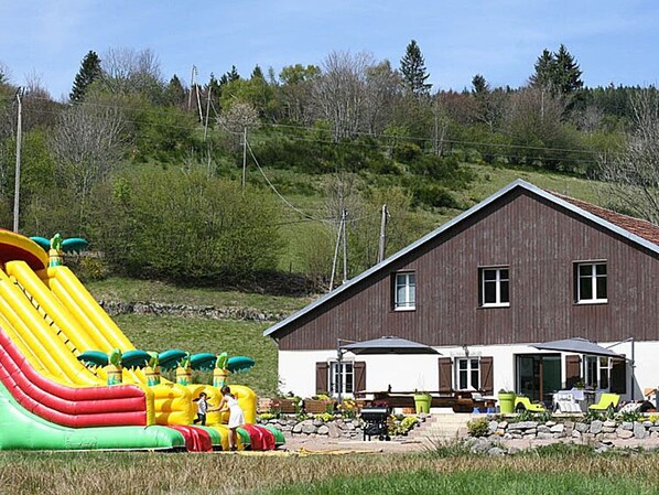 A two-story house with a brown roof and white walls, a patio with outdoor furniture, and a colorful inflatable slide in the foreground.