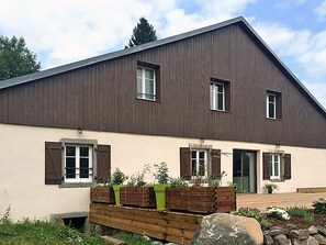 A modern two-story house with a sloped roof, wooden shutters, and a front porch with planters.