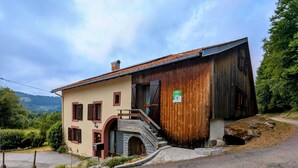 A rustic building with a stone staircase leading to a wooden door, surrounded by greenery and a clear sky.