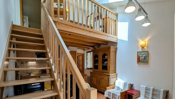 A multi-level wooden staircase leading to a loft bedroom with a bed and a desk.