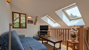 A cozy loft bedroom with a sloped ceiling, skylights, a bed, a TV, and a wooden table.