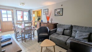 Ein Wohnzimmer mit grauem Sofa, einem Holztisch und einem Essbereich mit Tisch für zwei Personen.