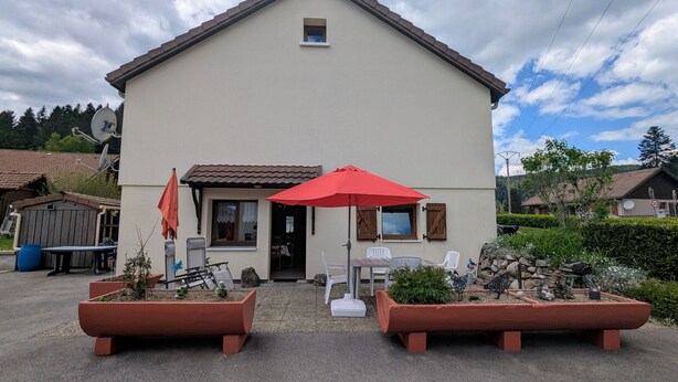 Ein zweistöckiges Haus mit Veranda, Satellitenschüssel und einer Sitzgruppe im Freien mit einem roten Sonnenschirm.