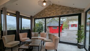 A modern interior with a stone ceiling, large windows, and a view of a red building outside. - Chalet spacieux dans les Hautes Vosges avec sauna, spa, terrain privé et accès facile aux commodités (Fresse-sur-Moselle)