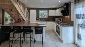 A modern kitchen with a wooden staircase, white cabinets, and a large island with bar stools. - Chalet spacieux dans les Hautes Vosges avec sauna, spa, terrain privé et accès facile aux commodités (Fresse-sur-Moselle)