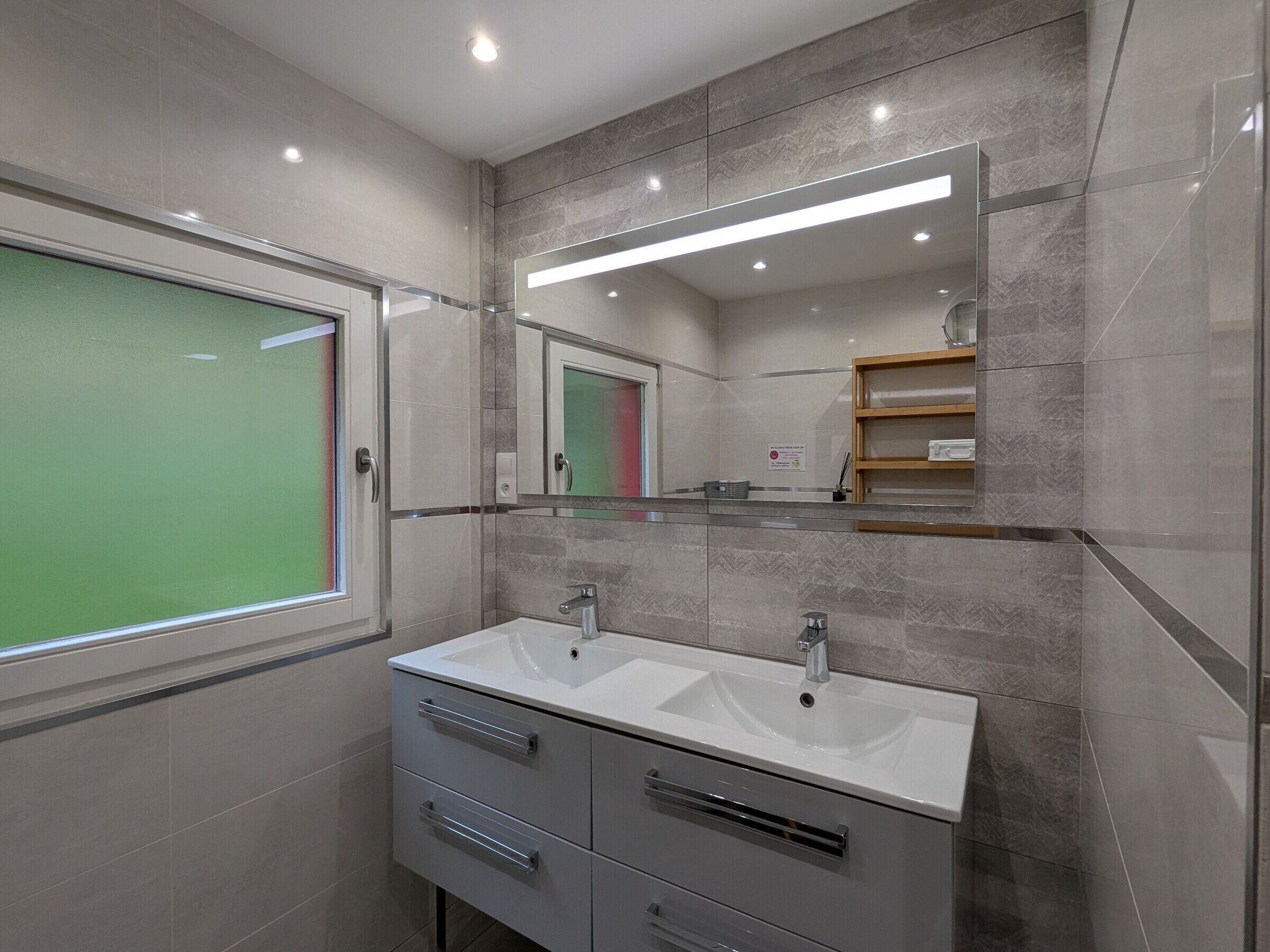 A modern bathroom with two sinks, a large mirror, and a window.