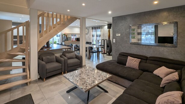 A modern living room with a staircase, a dining area, and a kitchen in the background. - Chalet spacieux dans les Hautes Vosges avec sauna, spa, terrain privé et accès facile aux commodités (Fresse-sur-Moselle)