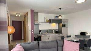 A modern apartment with a grey sofa, a dining table, and a kitchen area. - Chalet confortable avec sauna privé, grande terrasse et accès piscine - Montagne tranquille (Ferdrupt)