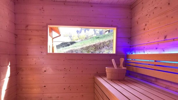 A wooden sauna with a bench, a window, and a stone container. - Chalet confortable avec sauna privé, grande terrasse et accès piscine - Montagne tranquille (Ferdrupt)