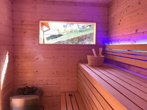 Una sauna de madera con un banco, una ventana y un recipiente de piedra.