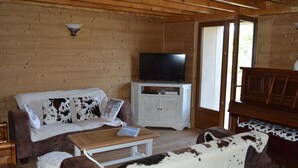 A cozy cabin interior with a wooden interior, a sofa with a cowhide cover, a television on a cabinet, and a piano. - Renovated 4-bedroom village house with lake view (Les Angles)