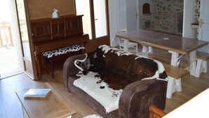A rustic cabin interior with a wooden dining table, a sofa with a cowhide cover, a piano, and a stone wall. - Renovated 4-bedroom village house with lake view (Les Angles)