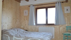 A wooden room with a bed, a chair, and a window with curtains. - Renovated 4-bedroom village house with lake view (Les Angles)