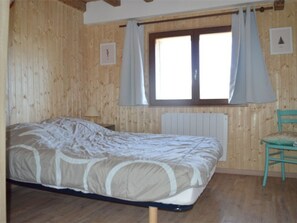 A wooden room with a bed, a chair, and a window with curtains.
