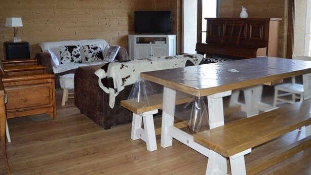 A rustic cabin interior with a wooden dining table, benches, a sofa with cowhide cover, a television, and a cabinet. - Renovated 4-bedroom village house with lake view (Les Angles)