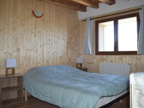 A wooden-paneled room with a bed, two bedside tables with lamps, a window with curtains, and a radiator. - Renovated 4-bedroom village house with lake view (Les Angles)