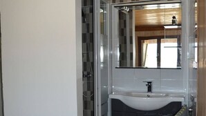 A bathroom with a white sink, dark cabinets, a glass shower enclosure, and a mirror above the sink. - Renovated 4-bedroom village house with lake view (Les Angles)