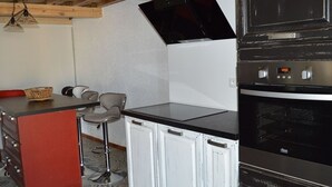 A compact kitchen with a built-in oven, a small dining area with a bar stool, and a red cabinet. - Renovated 4-bedroom village house with lake view (Les Angles)