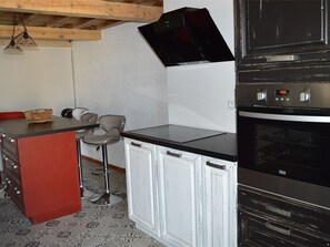A compact kitchen with a built-in oven, a small dining area with a bar stool, and a red cabinet.