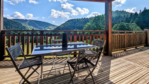 Um deck de madeira com mesa e cadeiras, com vista para uma paisagem montanhosa.